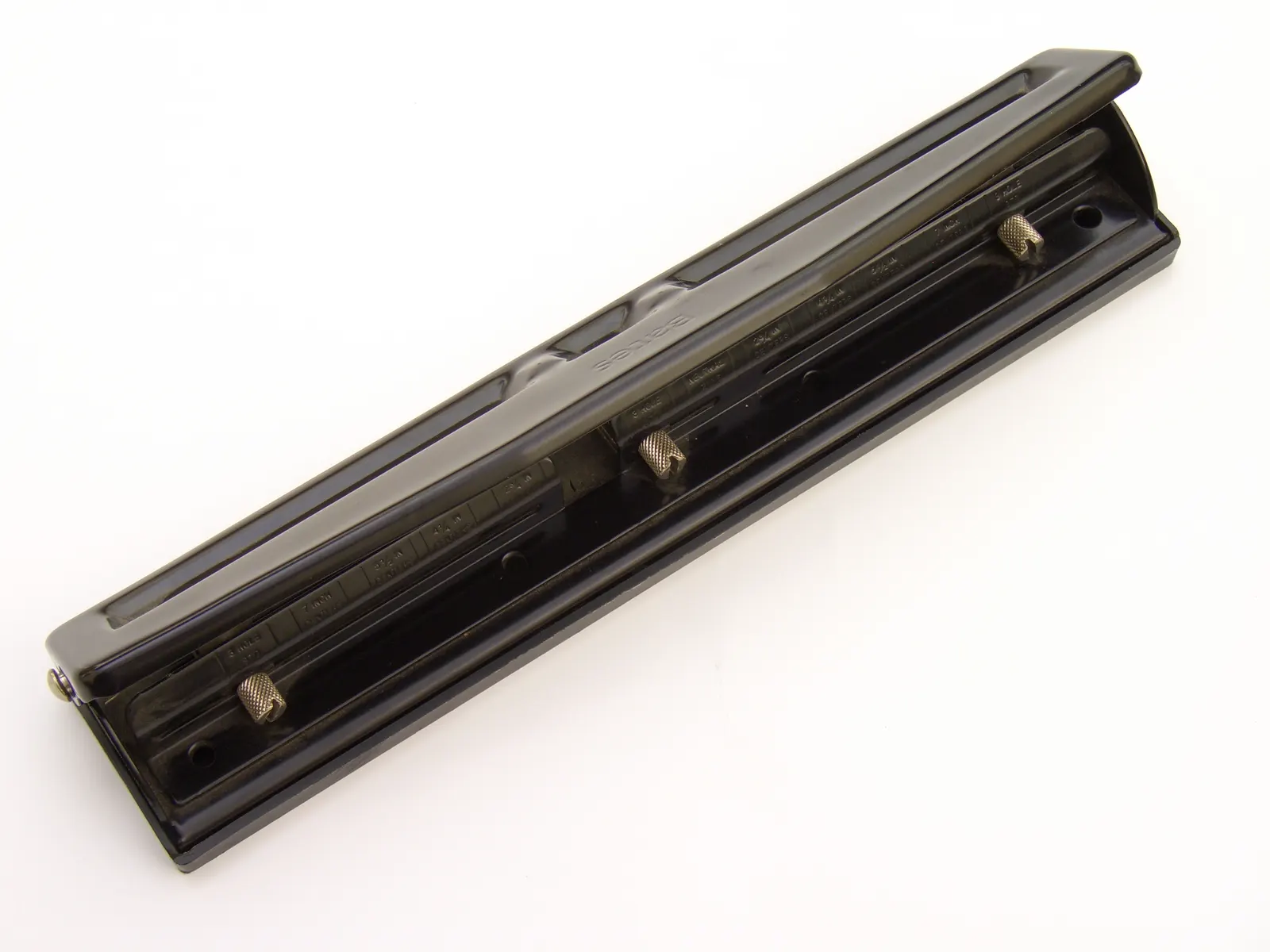 Black metal three-hole paper punch with brass adjusters on a white surface