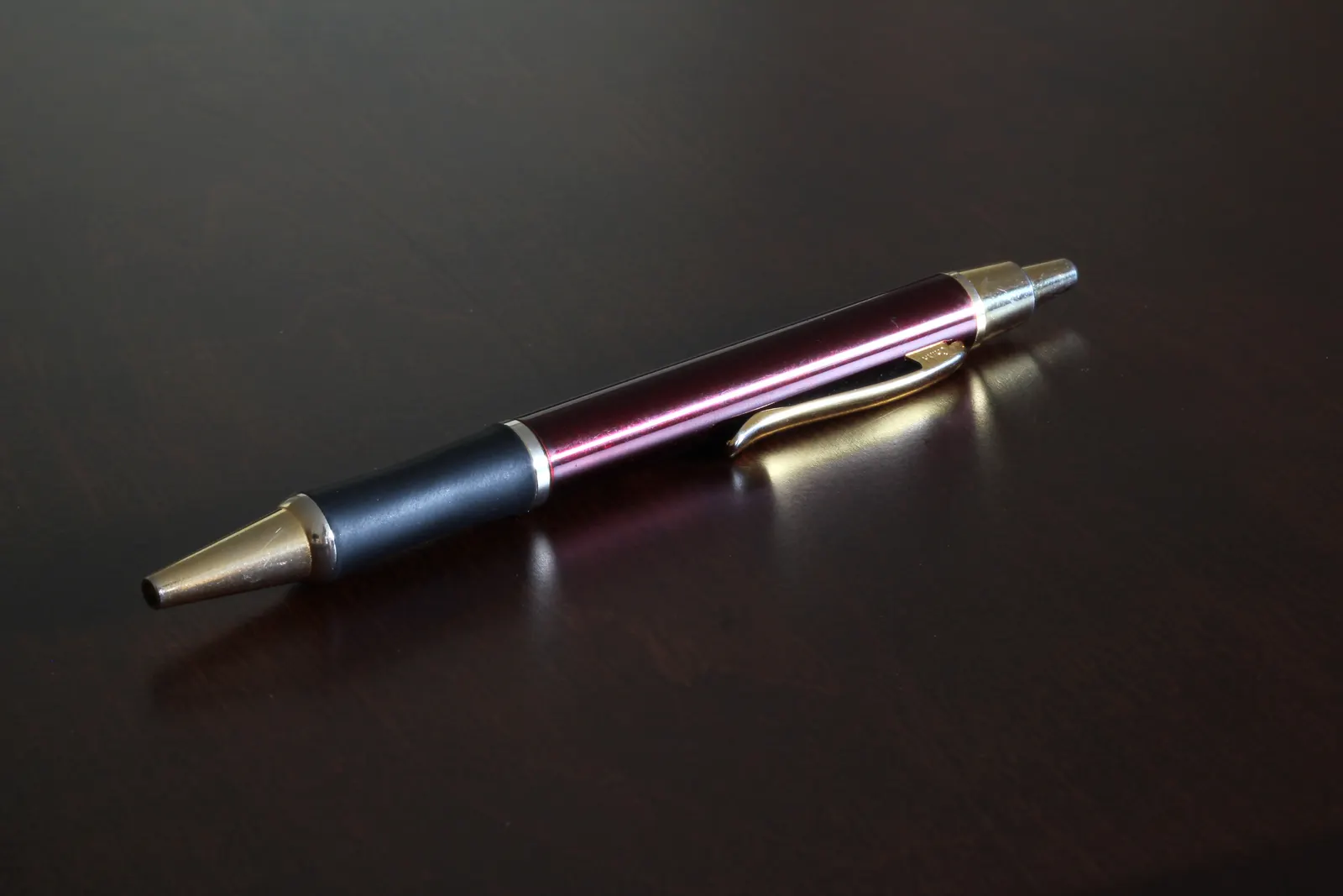Burgundy ballpoint pen with gold trim lying on a dark glossy wooden surface