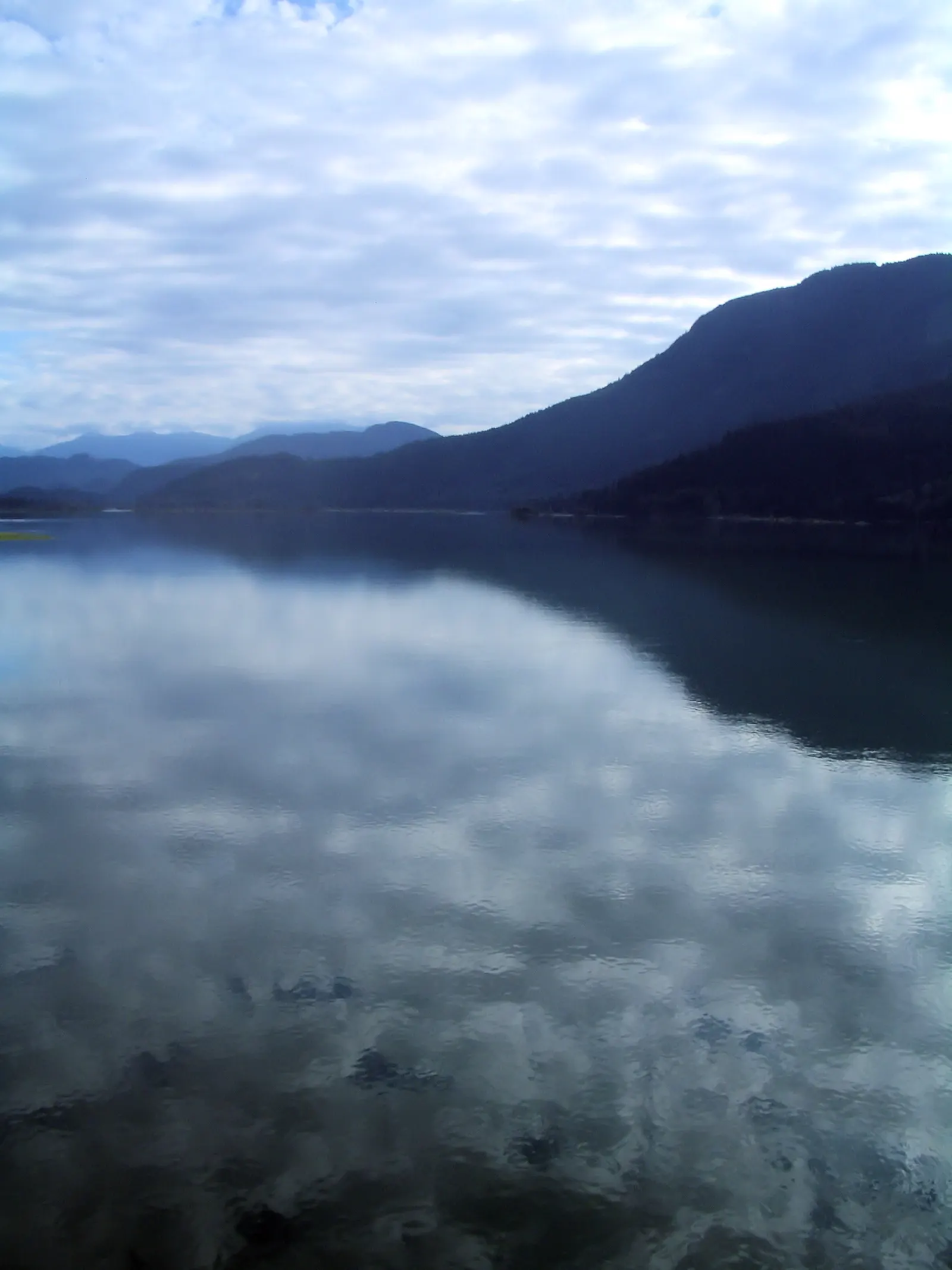 Calm lake reflecting clouds with forested mountains in the distance in British Columbia
