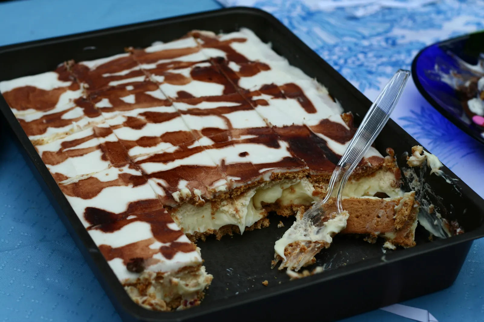 Baking pan of custard cream squares with chocolate drizzle and a fork in a cut piece