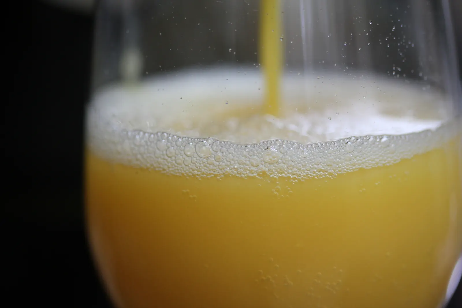 Close-up of orange juice being poured into a glass with foam and bubbles at the top