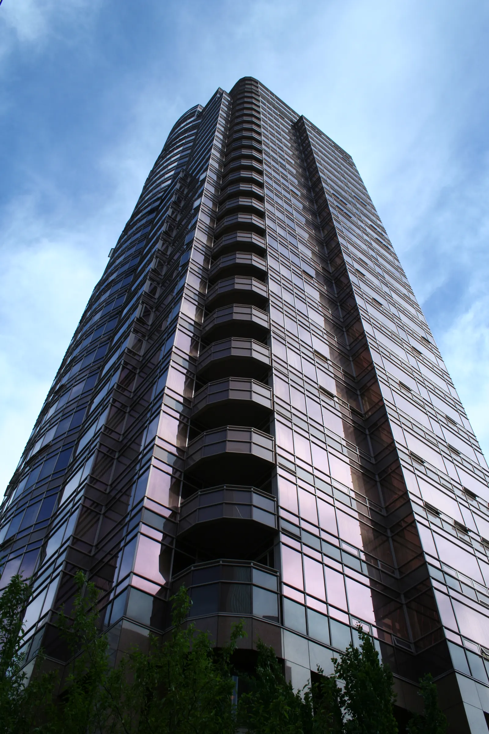 Tall high-rise with curved balconies and purple-tinted glass windows seen from below