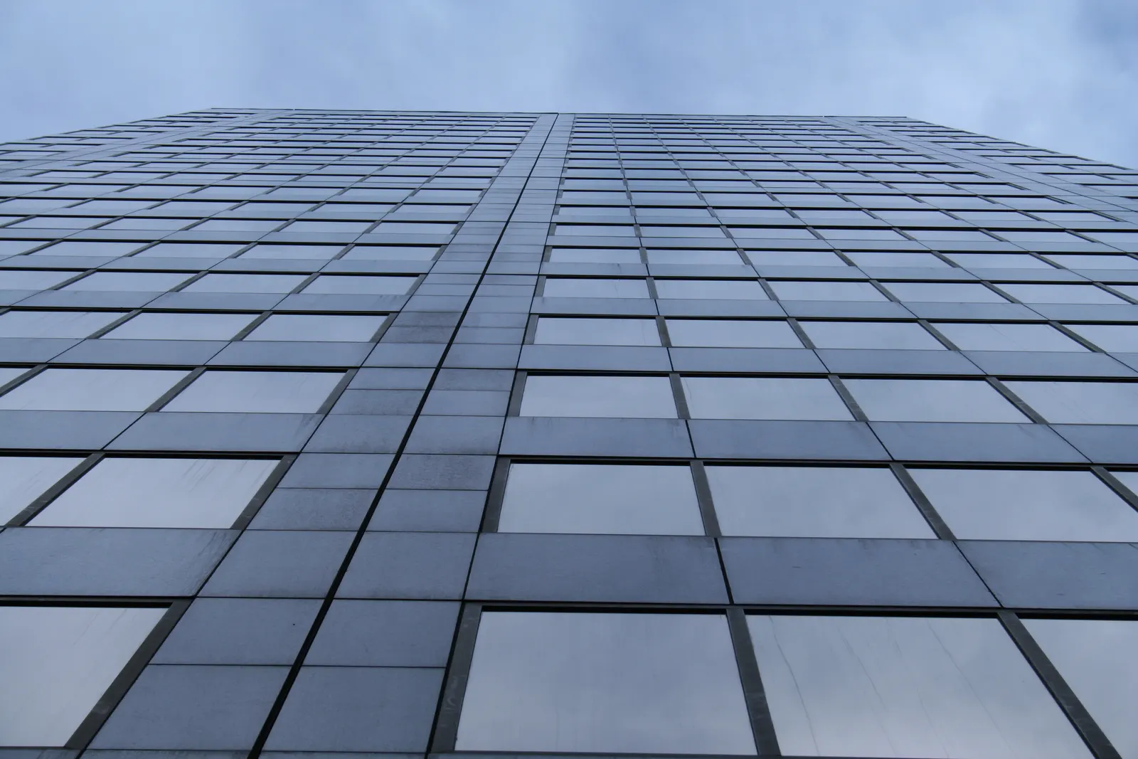Glass office tower facade viewed from below against a cloudy sky