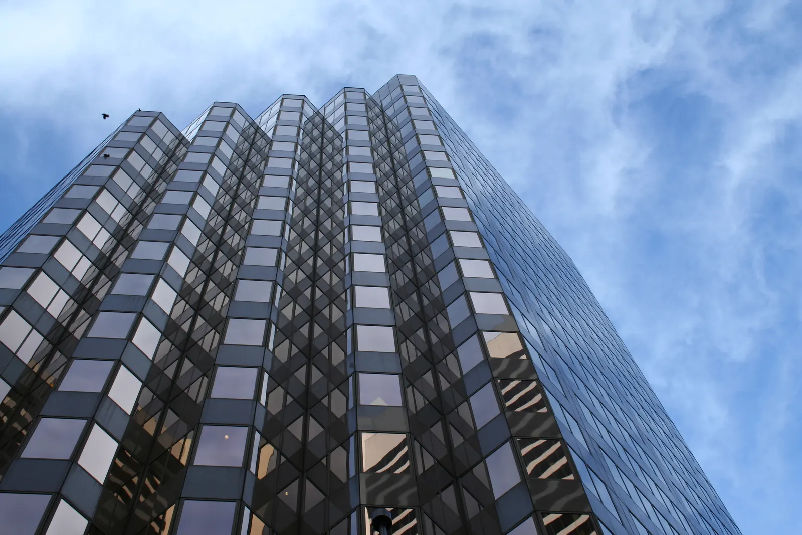 Low-angle view of a tall dark glass skyscraper against a blue sky with wispy clouds