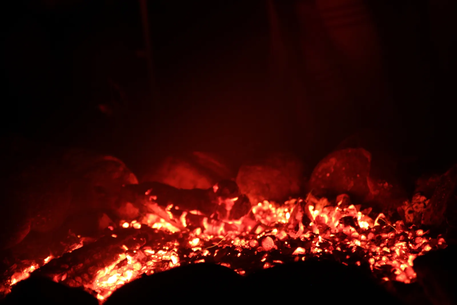 Glowing red and orange embers among charred logs in a dark fireplace
