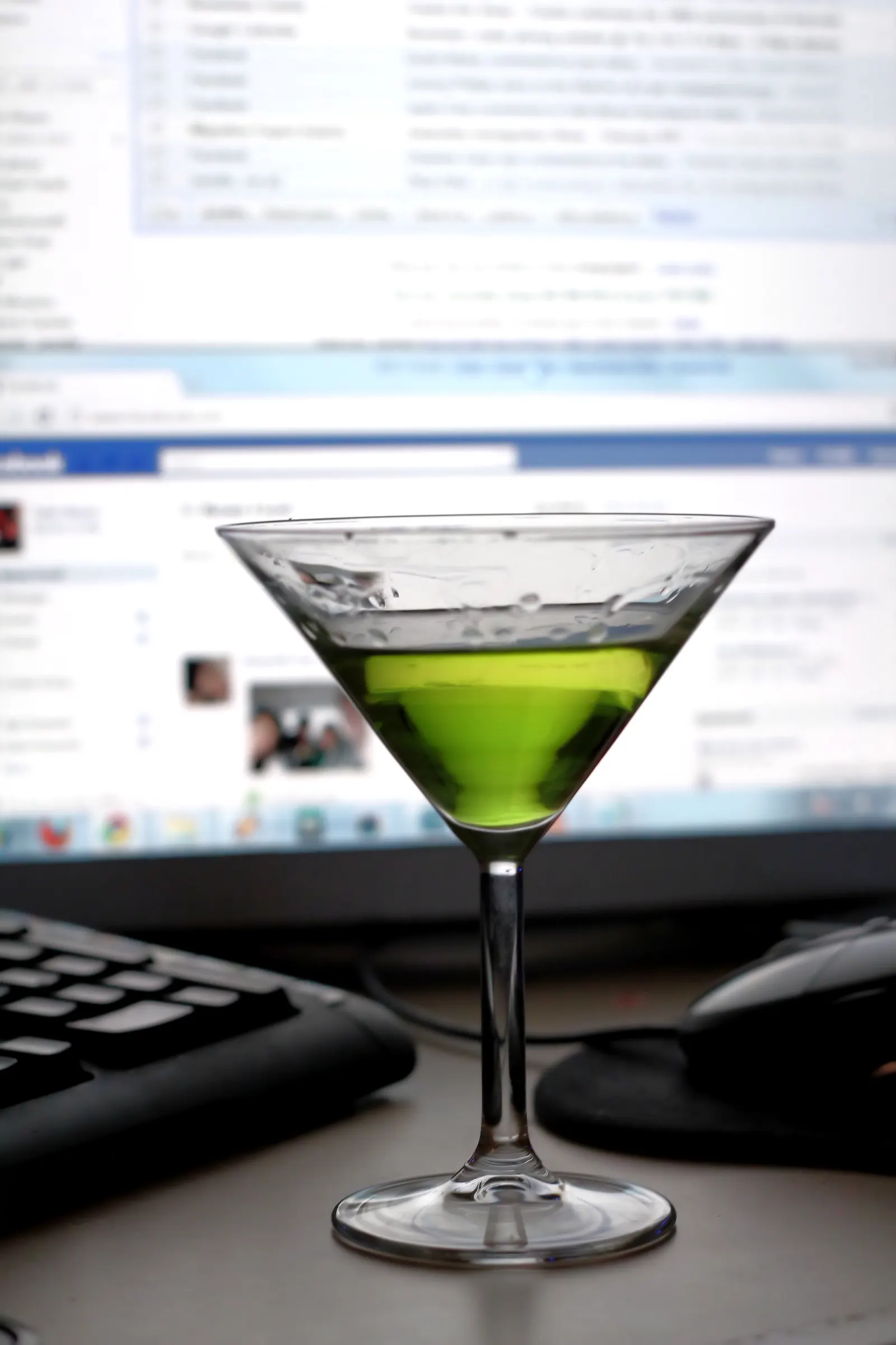 Green martini glass on a desk in front of a keyboard, mouse and blurred computer monitor