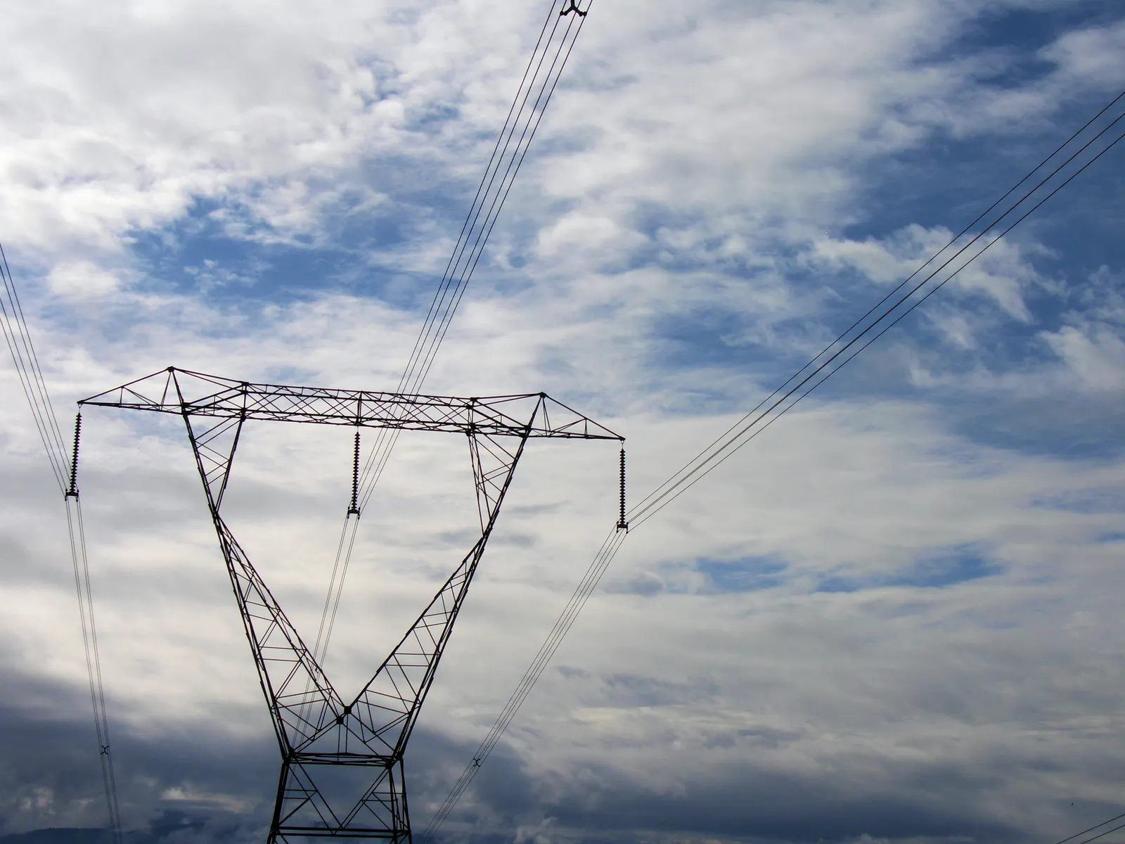 High voltage transmission tower and power lines against a cloudy blue sky