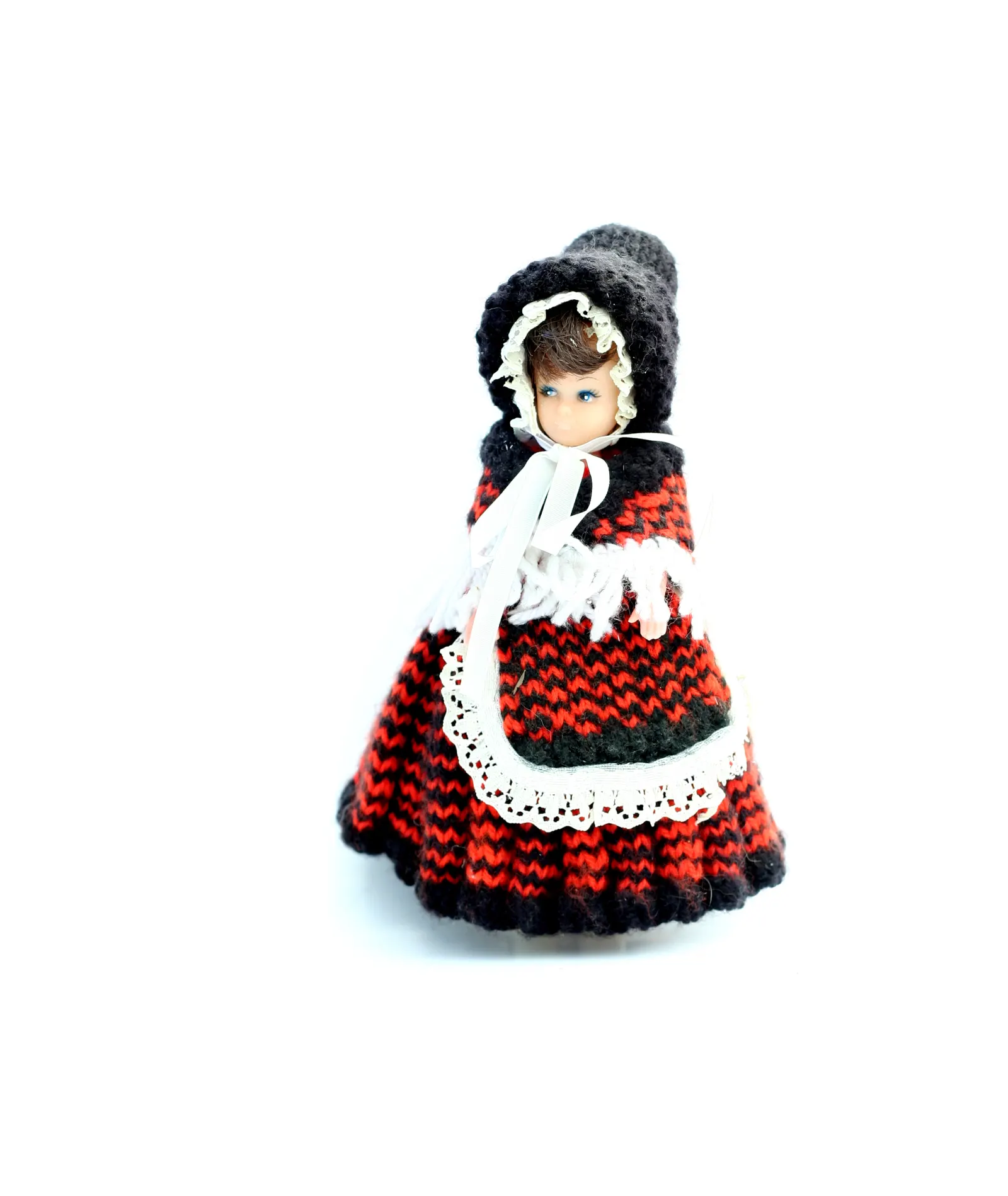 Doll in a knitted red and black wool dress with white lace apron and bonnet on white background
