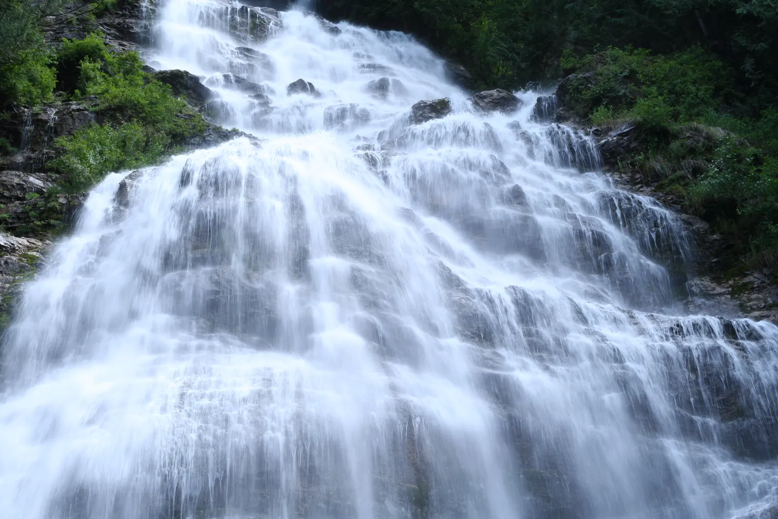 Silky long exposure waterfall cascading down rock ledges beside green foliage