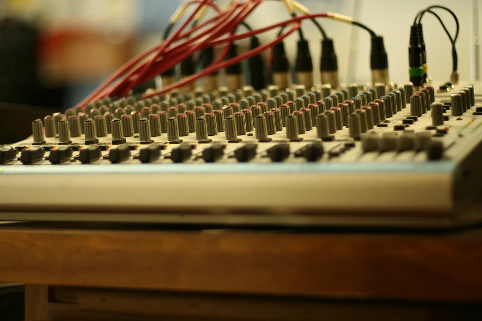 Low-angle view of an audio mixing console with rows of knobs and red XLR cables