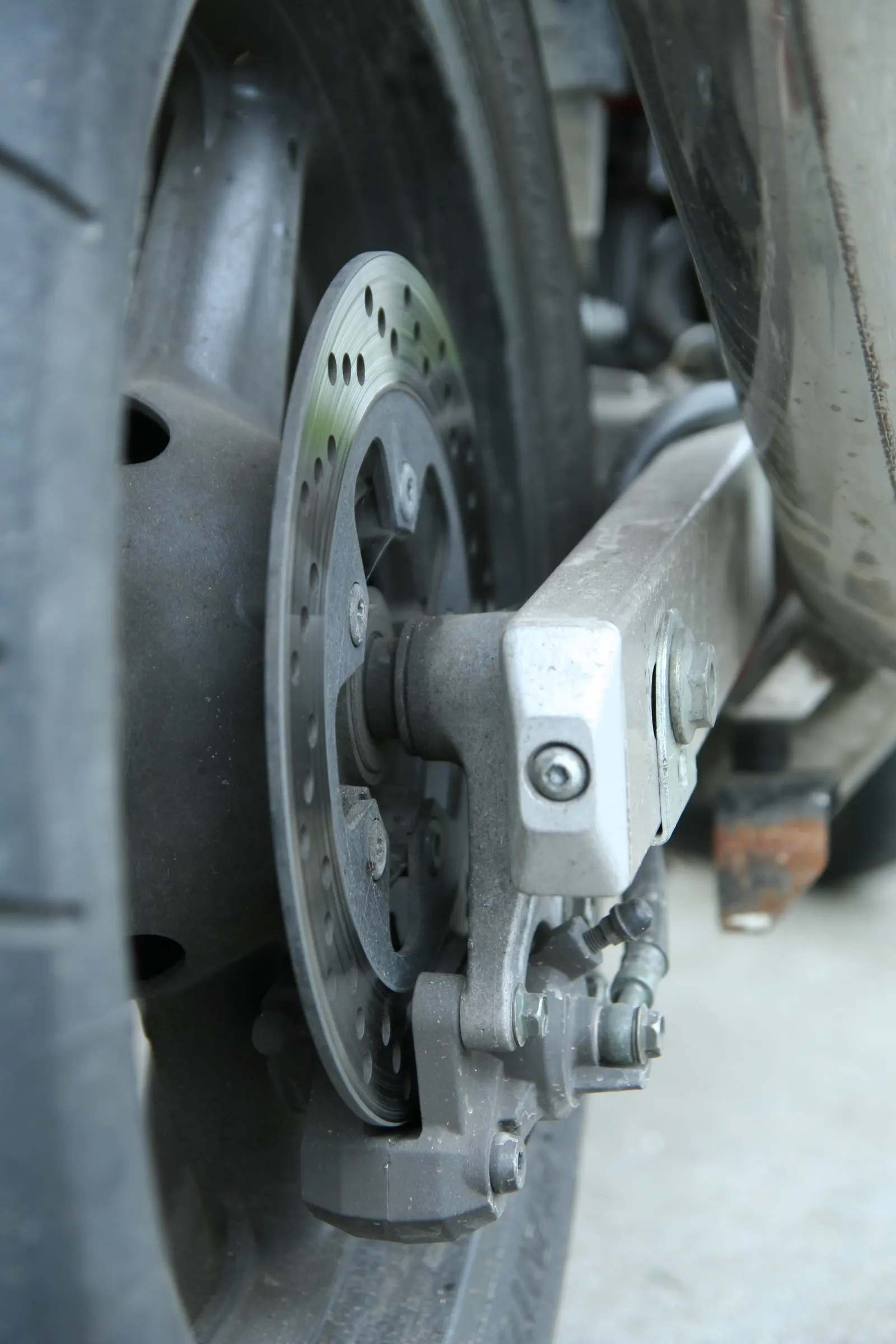 Close-up of a motorcycle rear wheel with a drilled brake disc and calliper