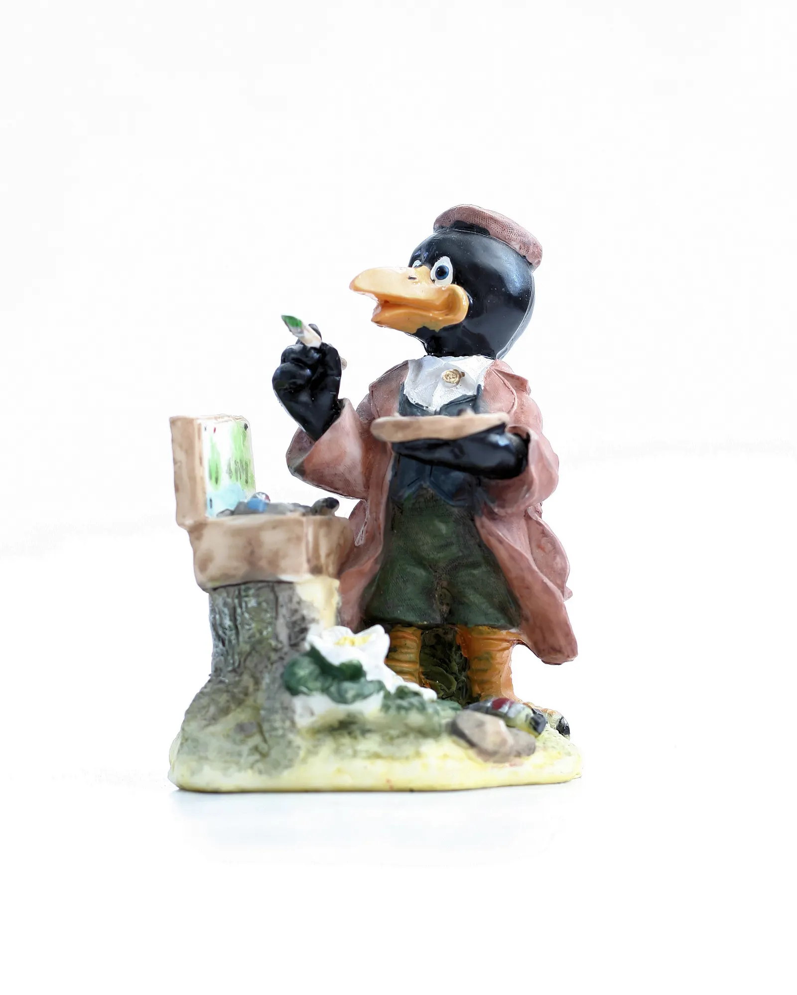 Figurine of a crow dressed as a painter holding a brush beside an easel, on white