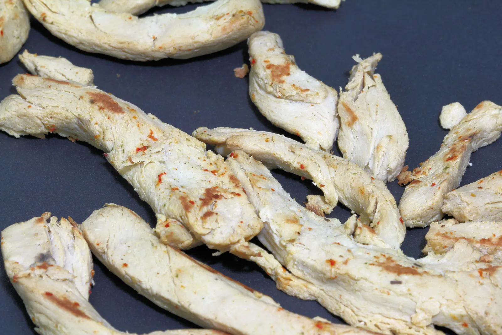 Seasoned seared chicken strips with chili flakes on a dark grey surface