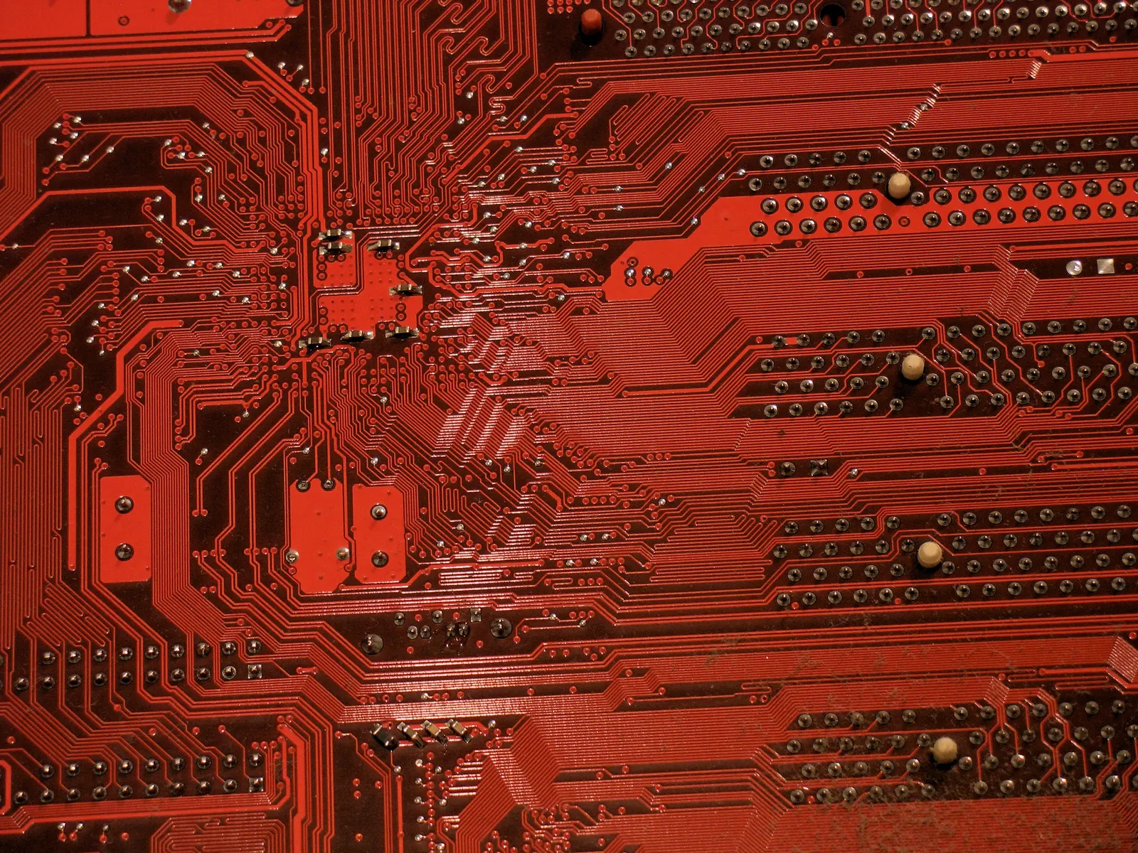 Close-up of a red circuit board with fine traces, solder points and through-holes