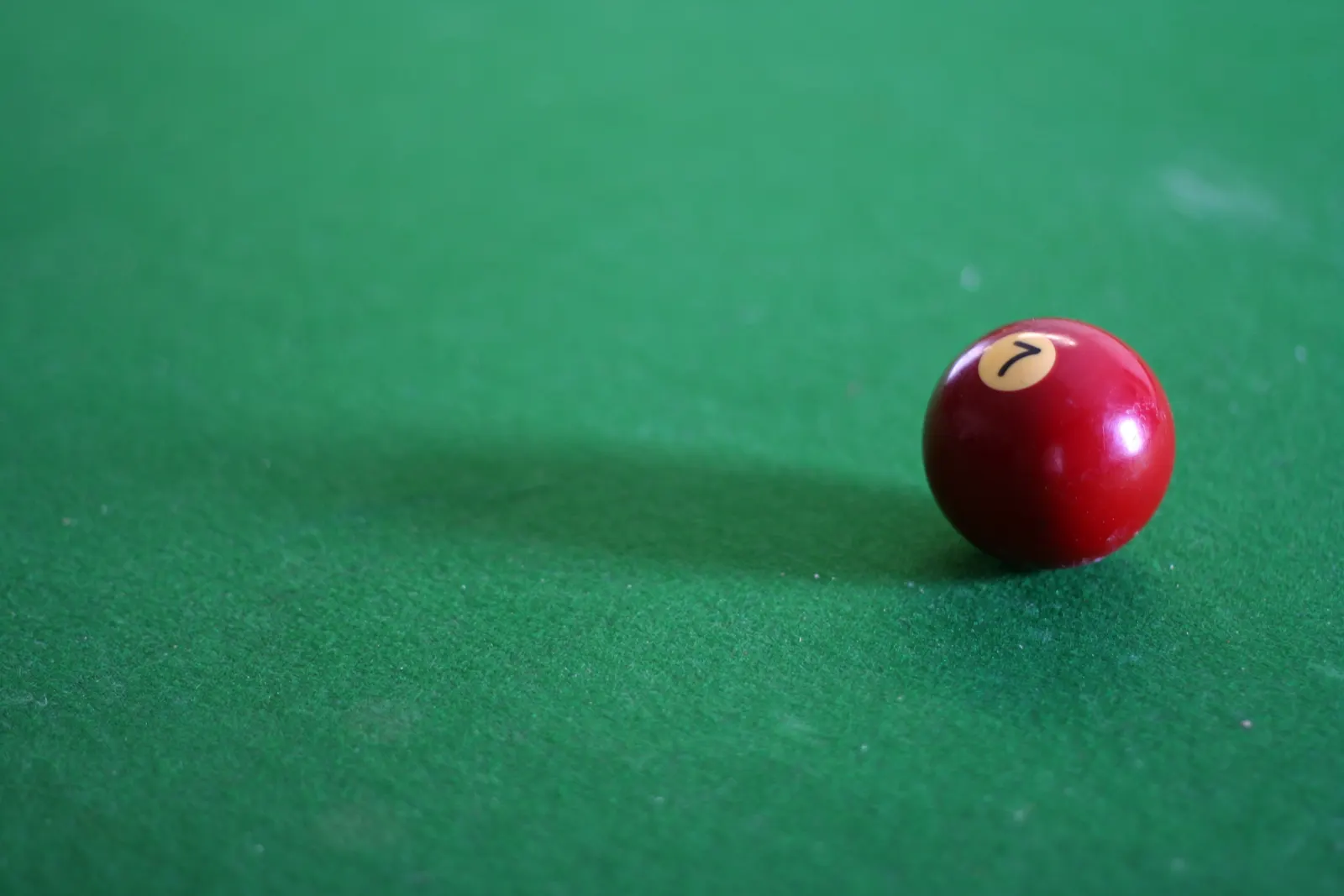 Red pool ball numbered 7 on a green billiard table with a soft shadow