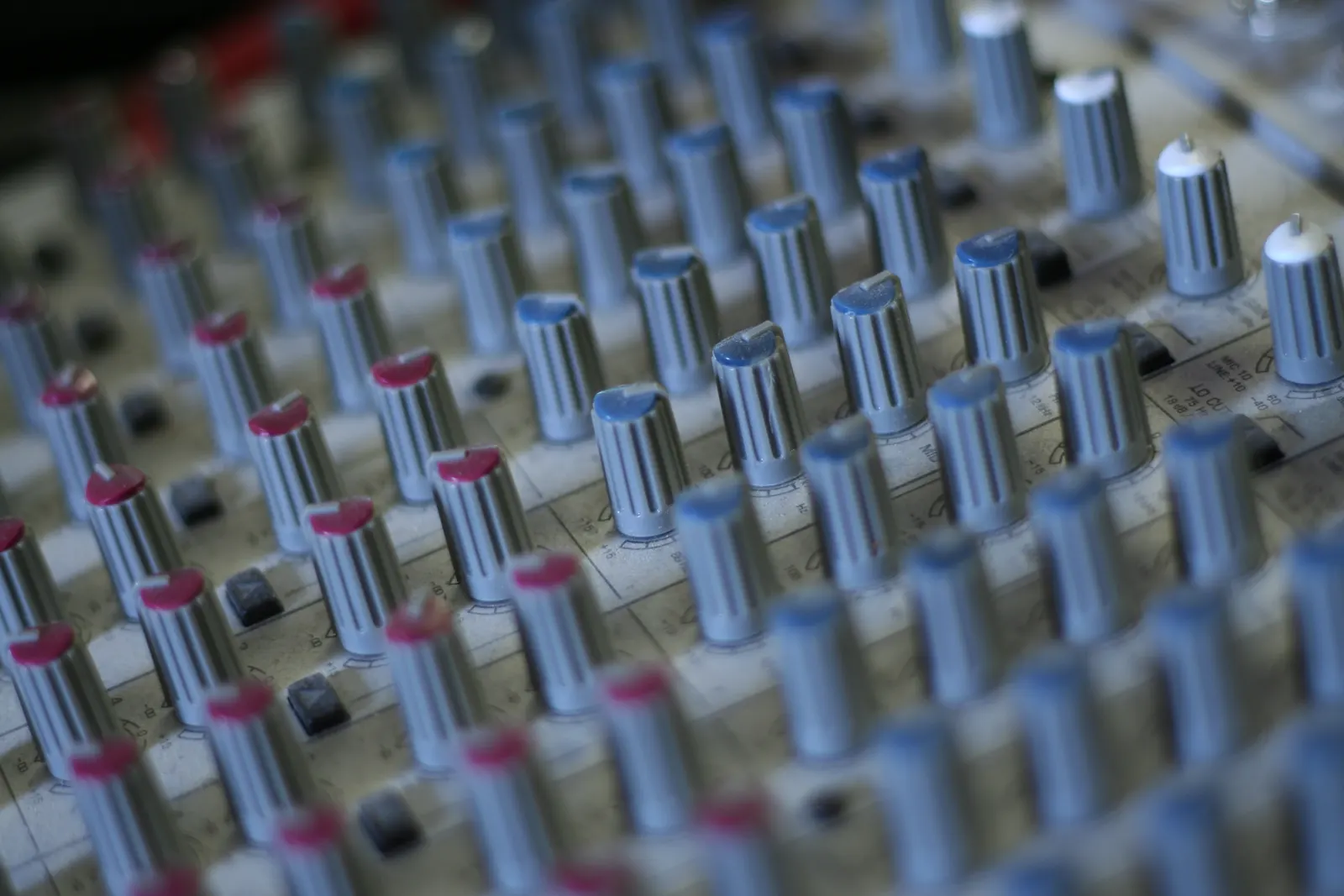Rows of grey and red knobs on an audio mixing console in shallow focus