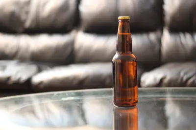 Amber beer bottle on a glass table in front of a blurred black leather sofa