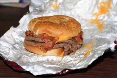 Bacon cheeseburger with melted cheese on a bun resting on crinkled foil wrapper