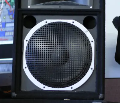 Front of a black carpeted PA speaker cabinet with a round woofer grille and horn tweeter