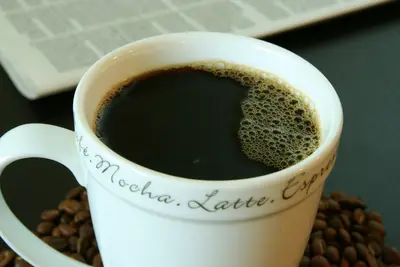 Close-up of black coffee in a white mug with coffee beans and a newspaper behind