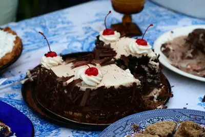 Chocolate cake with whipped cream rosettes, cherries and chocolate shavings on a patterned tablecloth