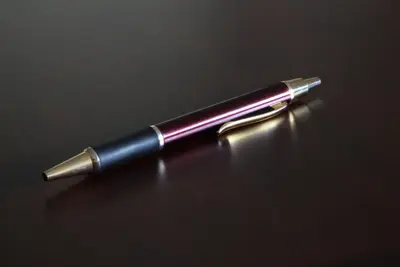 Burgundy ballpoint pen with gold trim lying on a dark glossy wooden surface