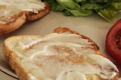Close-up of buttered toast on a plate beside lettuce and a tomato slice
