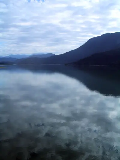 Calm lake reflecting clouds with forested mountains in the distance in British Columbia