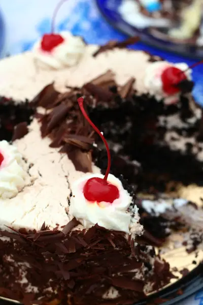 Close-up of a glossy red cherry on whipped cream atop a chocolate cake with a slice missing