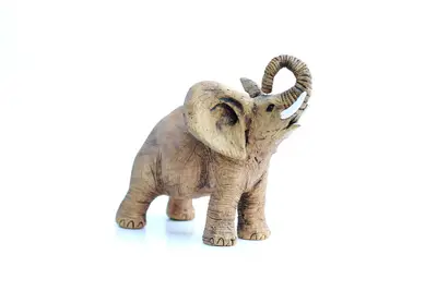 Small clay elephant figurine with raised curled trunk and white tusks on a white background