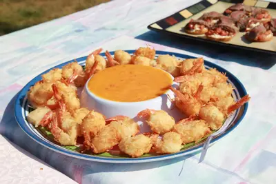 Plate of coconut shrimp surrounding a bowl of orange dipping sauce on an outdoor table