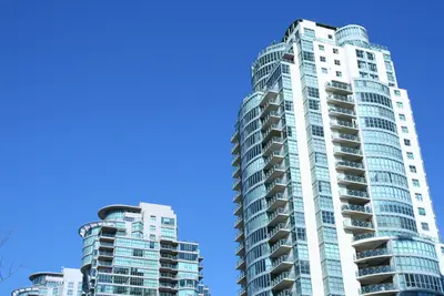 Tall curved white and glass apartment towers with balconies against a clear blue sky