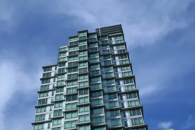 Tall glass residential tower with balconies seen from below against a blue sky with clouds
