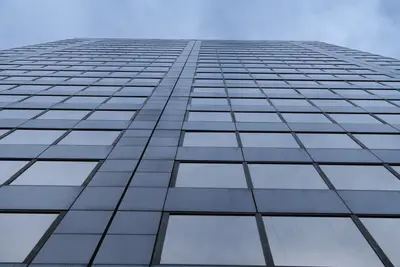 Glass office tower facade viewed from below against a cloudy sky