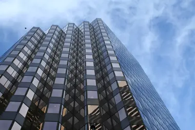 Low-angle view of a tall dark glass skyscraper against a blue sky with wispy clouds