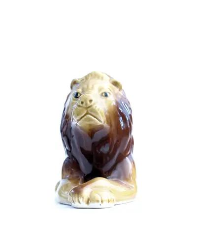Glossy brown and tan ceramic lion figurine lying down against a white background
