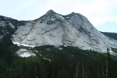 Grey granite mountain with snow patches rising above a dense evergreen forest