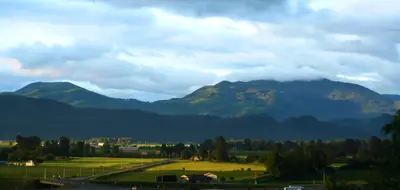 Green farm fields and buildings in a valley beneath forested mountains covered by low clouds