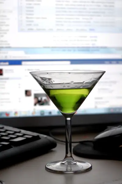 Green martini glass on a desk in front of a keyboard, mouse and blurred computer monitor