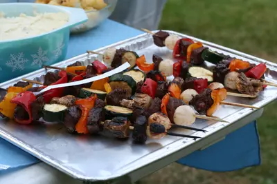 Grilled meat and vegetable skewers on an aluminium tray at an outdoor barbecue