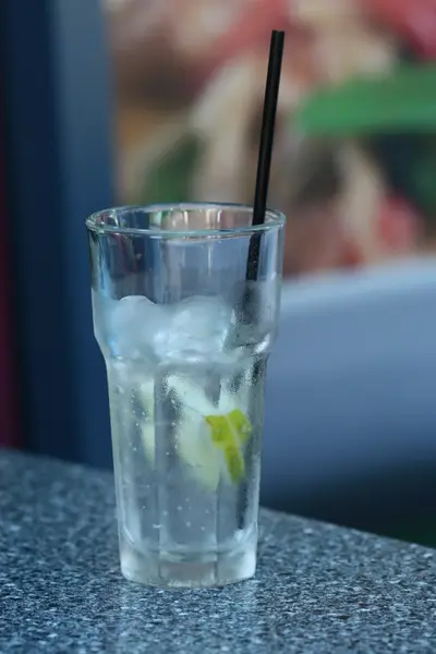 Glass of iced water with lime slice and black straw on a granite counter