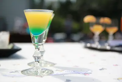 Layered yellow and green cocktail in a stemmed glass on an outdoor table with blurred glasses behind