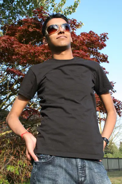 Young man in sunglasses, black t-shirt and jeans standing in front of a red maple tree