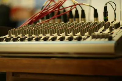 Low-angle view of an audio mixing console with rows of knobs and red XLR cables