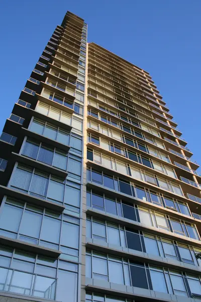 Modern glass high-rise apartment tower seen from below against a deep blue sky