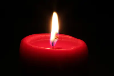 Lit red candle with a bright flame against a black background