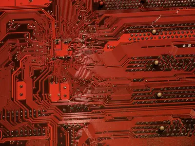 Close-up of a red circuit board with fine traces, solder points and through-holes