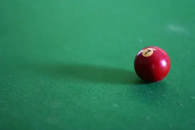 Red pool ball numbered 7 on a green billiard table with a soft shadow