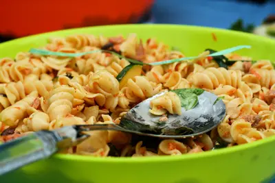 Spiral pasta salad with tomato and herbs in a bright green bowl with a serving spoon
