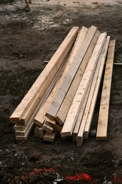 Stack of rough-cut wooden beams on muddy ground at a construction site